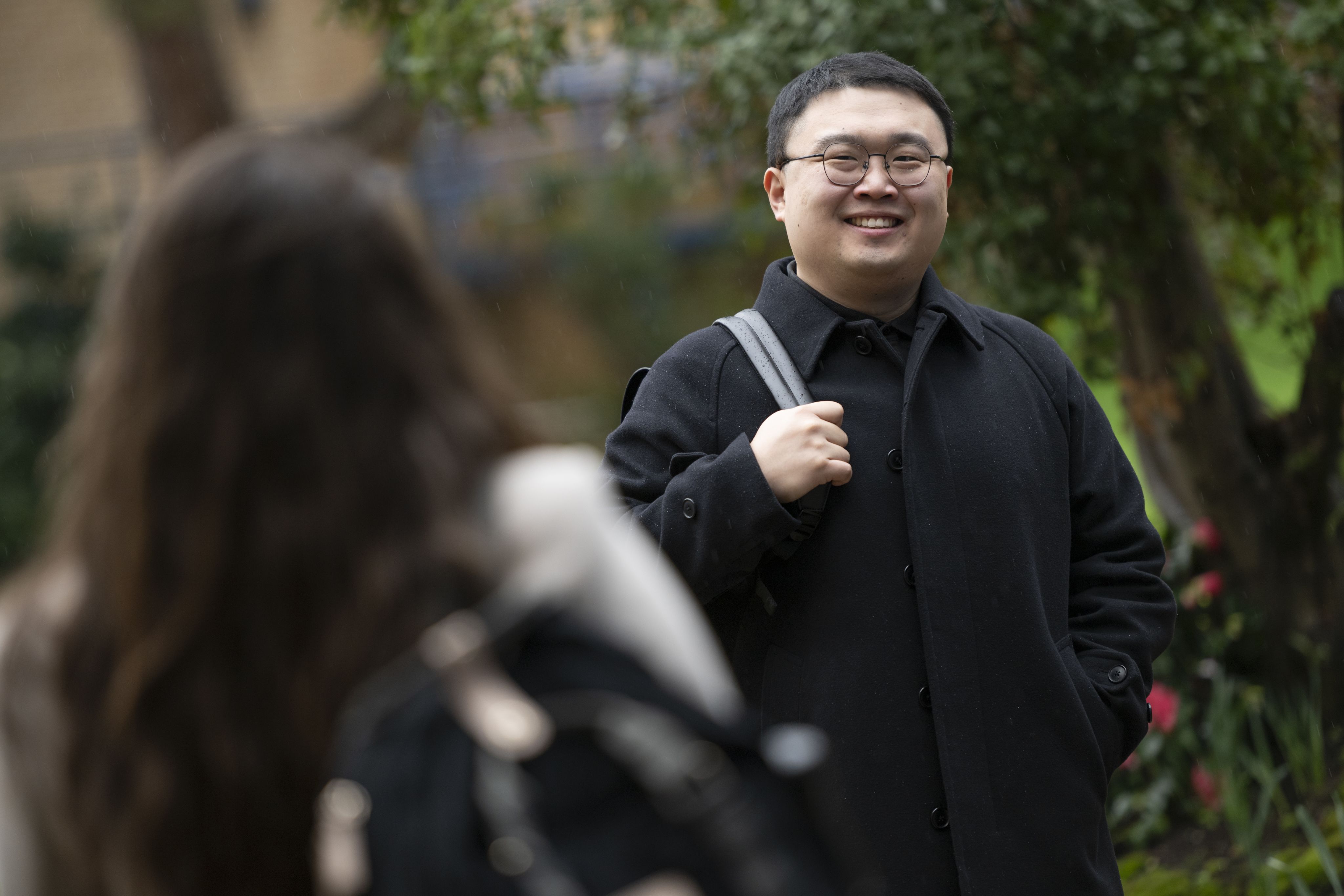 Frank smiles at a fellow student as he walks on campus with a bag on his shoulder