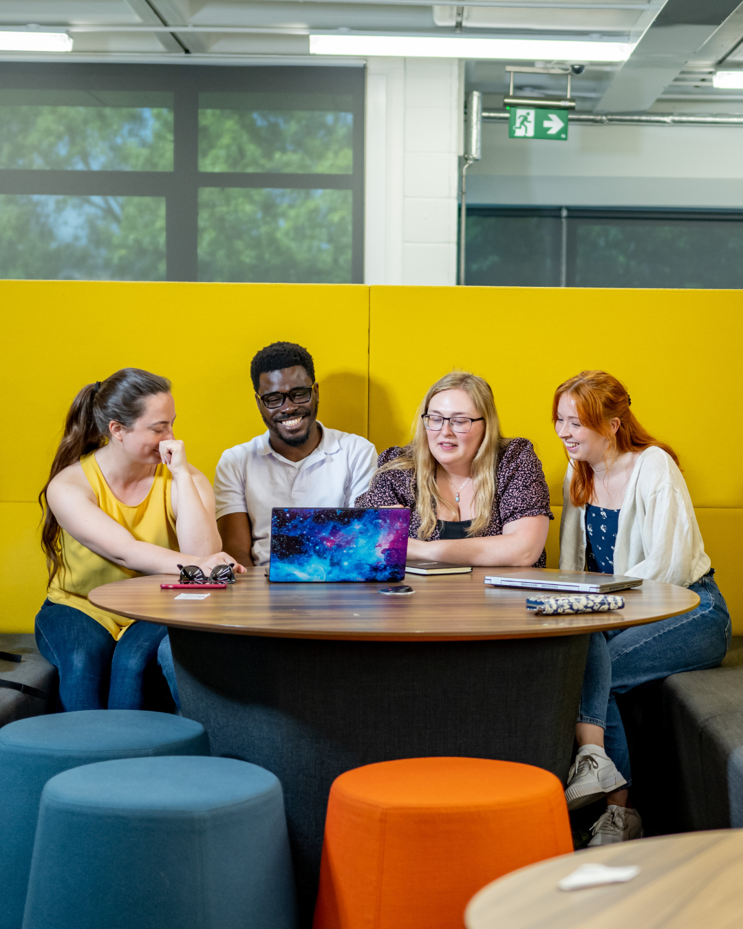 Four students sit around a laptop in the library