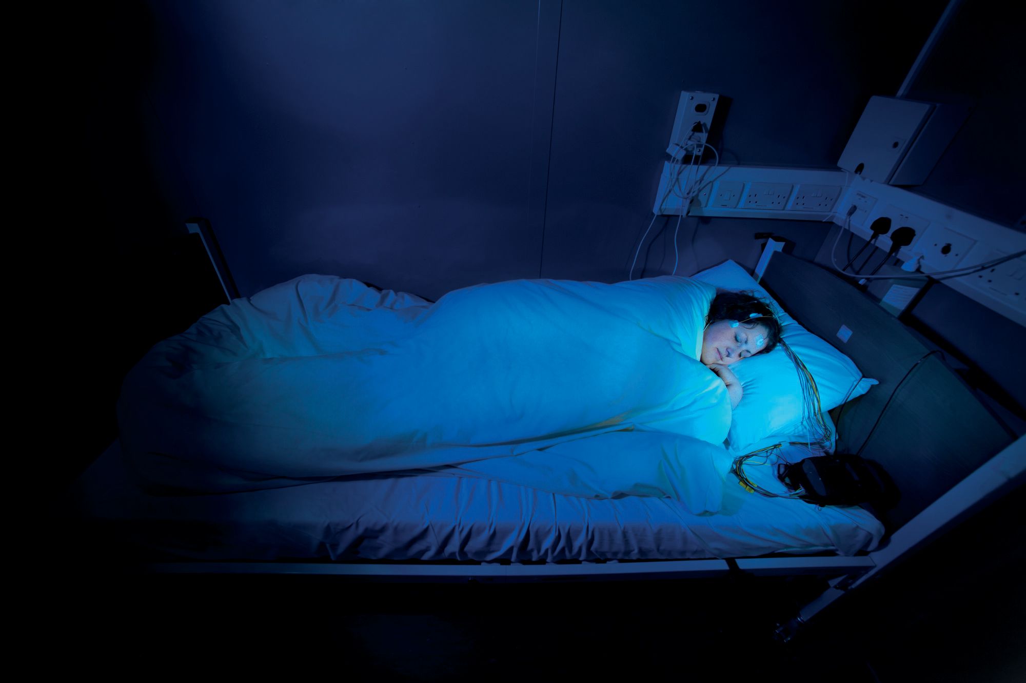 A person sleeps with wires attached to their head as part of sleep research at the University of Surrey